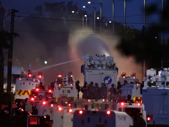 Water cannons being fired in a street amid numerous police vehicles and officers in riot gear